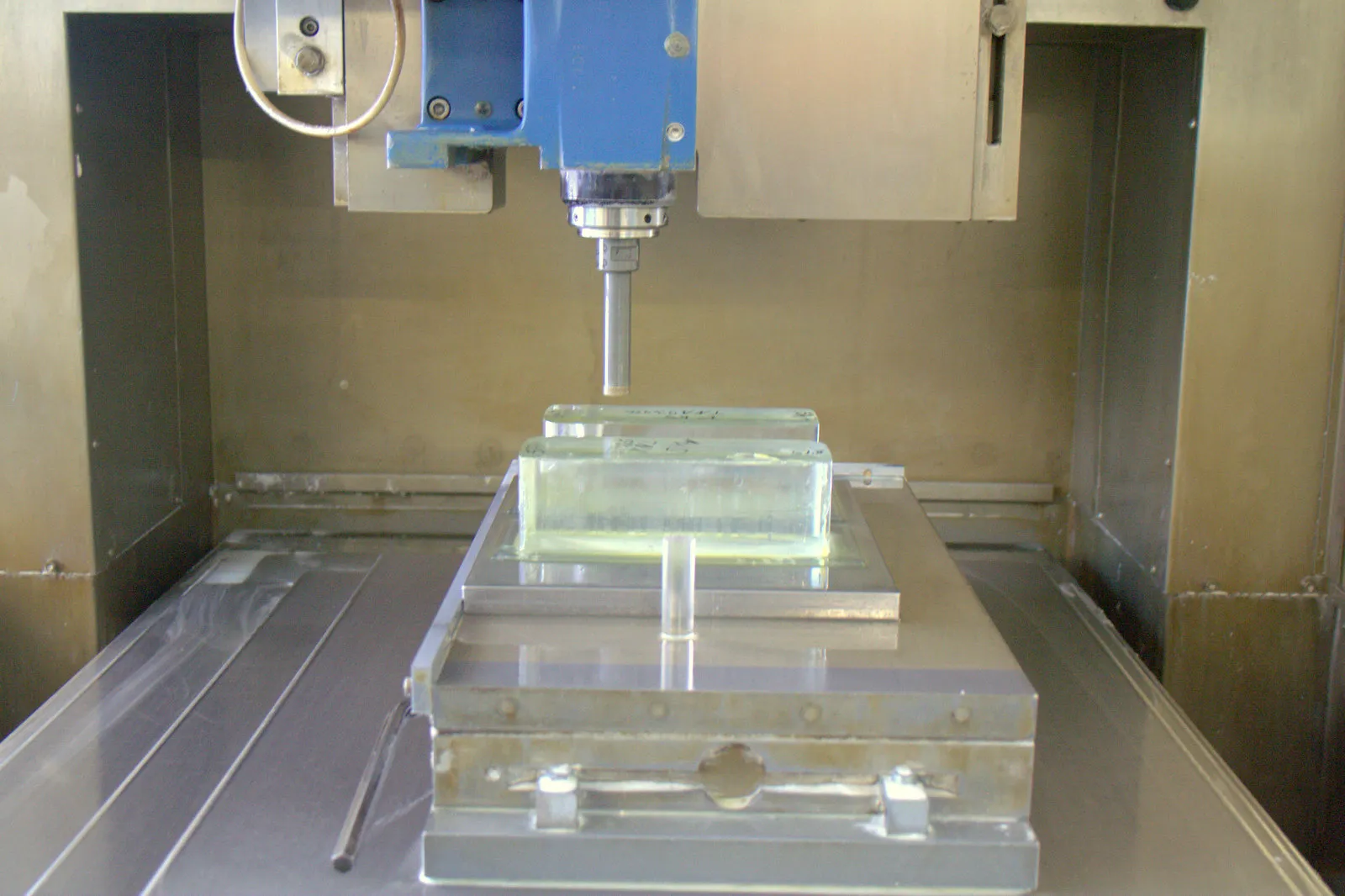 Glasblock auf der Spannvorrichtung einer CNC-Bohrmaschine, darüber die Spindel mit dem Bohrer