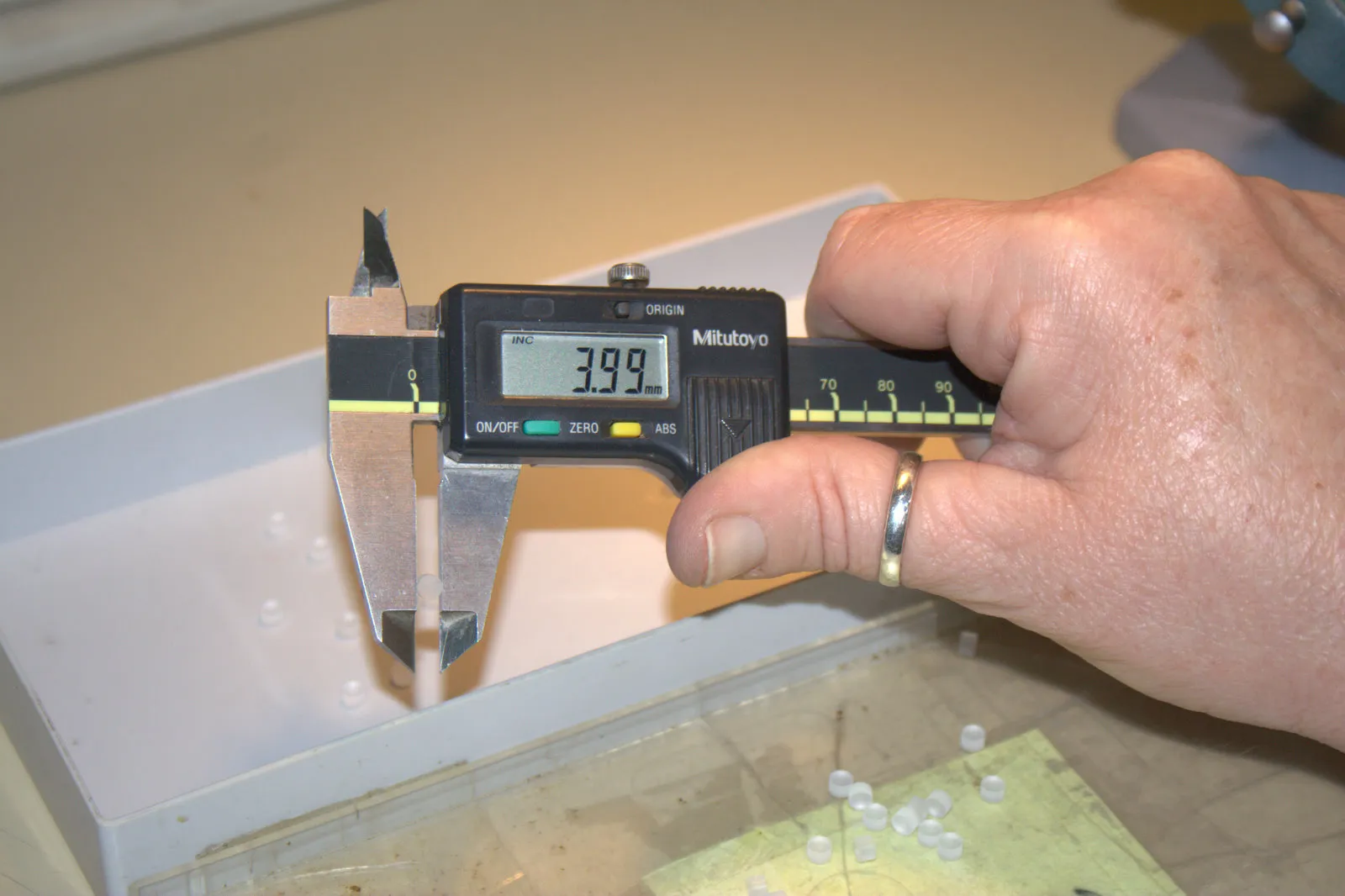 Digitaler Messschieber zeigt 3,99 mm beim Messen eines kleinen Glasteils, daneben weitere Glasteile in einer Schale