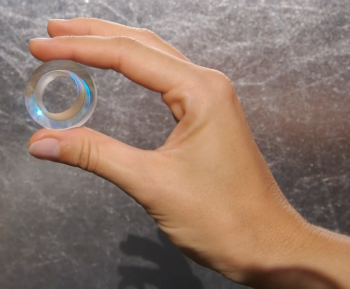 Eine Hand hält einen ringförmigen Glas-Rohling vor dunklem Steinhintergrund
